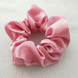 Close-up of pink satin silk scrunchie with soft fabric texture on grey felt background