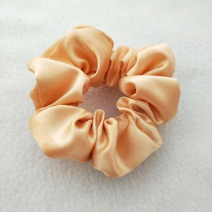 Detail of a smooth apricot satin scrunchie showing glossy silk texture and durable elastic
