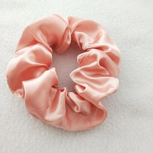 Close-up of soft pink satin silk hair scrunchie texture on a clean white background