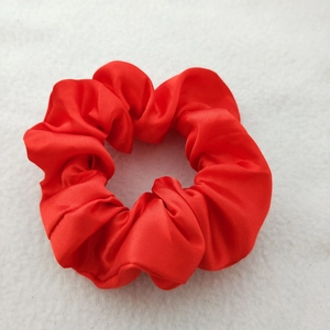 Detailed close-up of a red satin silk scrunchie on a soft white textured background