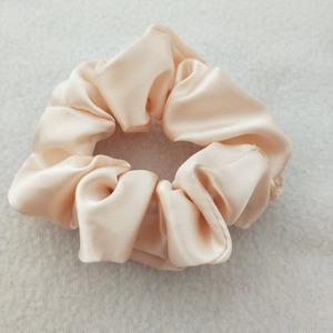 Detail view of champagne satin fabric texture and soft luster on a high-elastic scrunchie