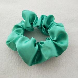 Macro detail of glossy green satin scrunchie showing smooth texture and soft folds