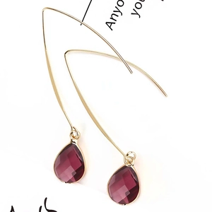 Macro shot of purple teardrop crystal earrings with gold plated hooks on a white background