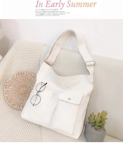 Detail van witte canvas crossbodytas met voorzakken en een brede schouderriem