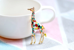 Close-up of a colorful enamel giraffe brooch with gold-tone finish on a white cup