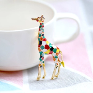 Golden giraffe brooch with colorful enamel pattern leaning on a white ceramic cup