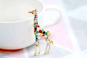 Detail of a gold giraffe brooch with colorful enamel patterns leaning on a white cup