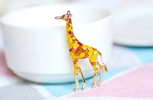 Detail of cute giraffe brooch in gold alloy and colorful enamel on a soft background