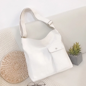 Minimalistische witte canvas schoudertas met brede riem en voorvak op een bank