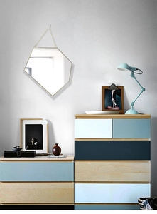 Detail of a minimalist gold pentagon mirror with elegant chain hanging on a grey wall