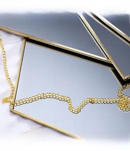 Detalle de espejo hexagonal dorado con cadena metálica sobre fondo de tela blanca