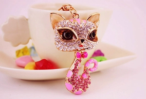 Close-up of cute golden fox keychain with pink rhinestones and a bow on a white cup
