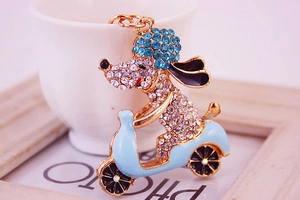 Detail of crystal rhinestone dog riding a blue motorcycle keychain in gold plating
