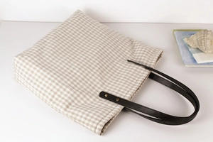 Detail of gingham tote bag with black leather handle and metal rivet reinforcement
