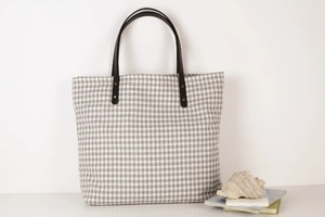 Detail of gingham canvas tote bag featuring premium leather handles and rivet accents