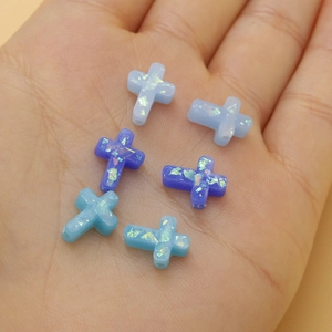 Cross-shaped synthetic opal beads with fire flash effect held in hand for scale
