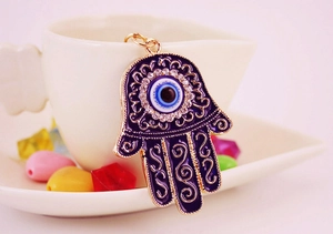 Close-up of purple Hamsa Hand keychain with crystal rhinestones on a coffee cup