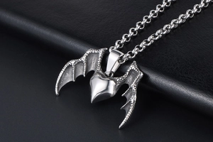 Detailed view of gothic silver heart pendant with dragon wings on a black leather surface