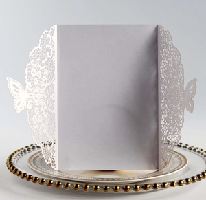 Macro detail of white laser-cut butterfly invitation card on decorative golden rimmed plate