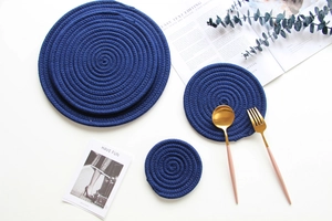 Detail of dark blue woven cotton coasters with spiral braided texture and gold cutlery