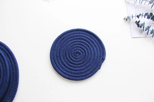 Detailed top view of a dark blue braided cotton rope coaster on a clean white table