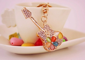 Detailed close-up of a golden guitar keychain with colorful cat eye stones and rhinestones