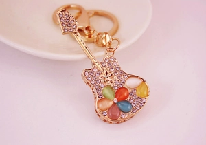 Detailed view of a gold guitar keychain with colorful rhinestones on a white ceramic plate