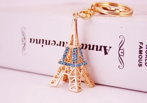 Gros plan du porte-clés Tour Eiffel doré orné de strass bleus sur un fond blanc épuré