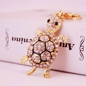 Golden metal turtle keychain with sparkling crystal rhinestones on pink background