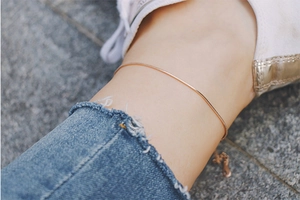 Close-up of minimalist rose gold snake chain anklet worn on ankle with white sneakers
