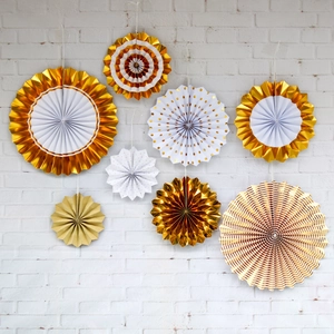Set of 8 gold and white decorative paper fans with stripes and dots on a white brick wall