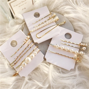 Detailed view of gold geometric pearl hair clip set displayed on soft white plush background