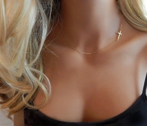 Gros plan d'un collier croix doré minimaliste au design latéral sur un mannequin femme