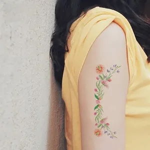 Detail of colorful floral temporary tattoo showing orange and pink flowers on woman arm