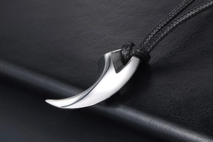 Macro shot of polished silver claw pendant with black woven cord on leather surface