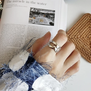 Detail of minimalist 925 sterling silver knotted ring on finger with aesthetic background