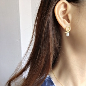 Detail view of gold twisted hoop earrings with teardrop pearls on a model's ear