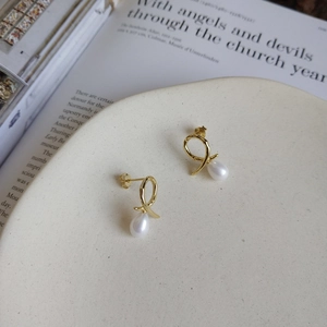 Close-up of golden drop pearl earrings on a ceramic plate with vintage book background