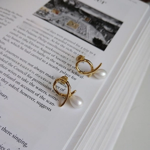 Detail of 925 silver irregular gold wire earrings with white teardrop pearls on a book