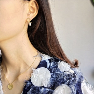 Detail of irregular gold pearl earrings and heart necklace worn on a model's neck