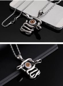 Macro shot of silver snake pendant with brown devil eye on a black laptop surface