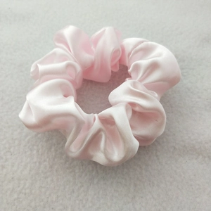 Detail of pink satin scrunchie showing glossy silk texture and pleated elastic design