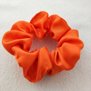 Detailed view of glossy orange satin scrunchie with soft folds on white texture