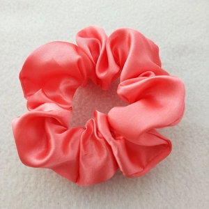 Close-up of pink satin silk scrunchie with elegant pleated texture on a soft background