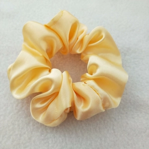 Close-up of a yellow satin scrunchie showing smooth silk texture and ruffled fabric design