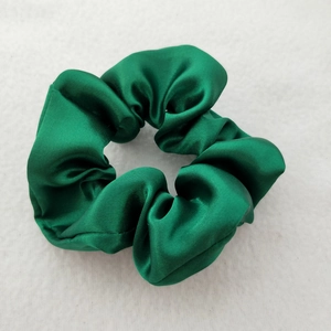 Detailed view of the glossy green satin silk scrunchie on a white textured background