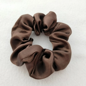 Close-up of brown satin scrunchie showing smooth texture and glossy finish on white background