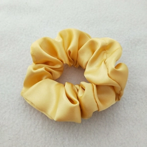 Close-up of bright yellow satin scrunchie showing smooth texture and high elasticity