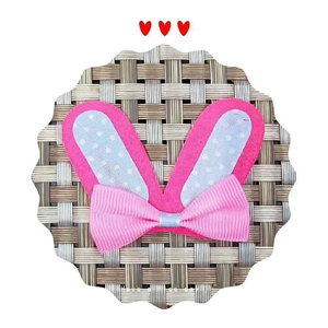 Pink felt rabbit ears hair accessory with blue polka dot bow on gray woven mat