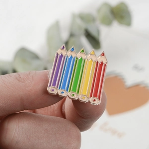 Detail of colorful rainbow pencil enamel brooch with gold trim held between fingers